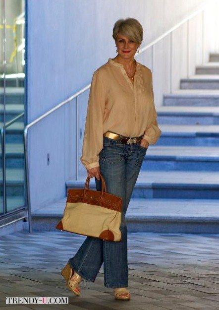 Бежевая блузка в сочетании с расклешенными джинсами на женщине среднего возраста